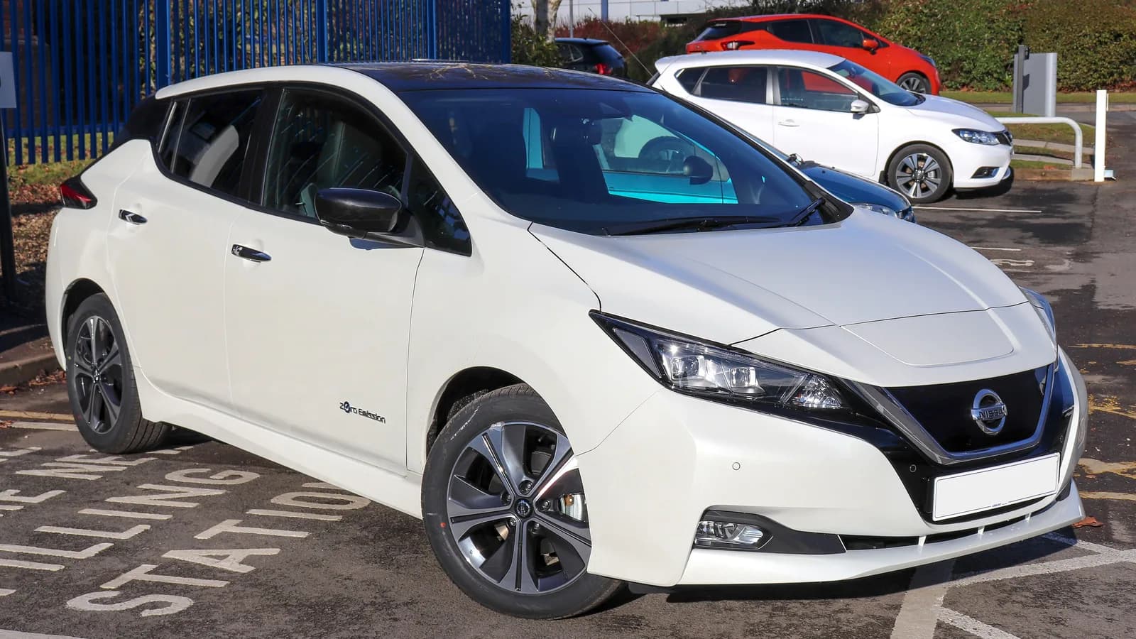 A white Nissan Leaf parked in an open car park, seen from the front three-quarter angle