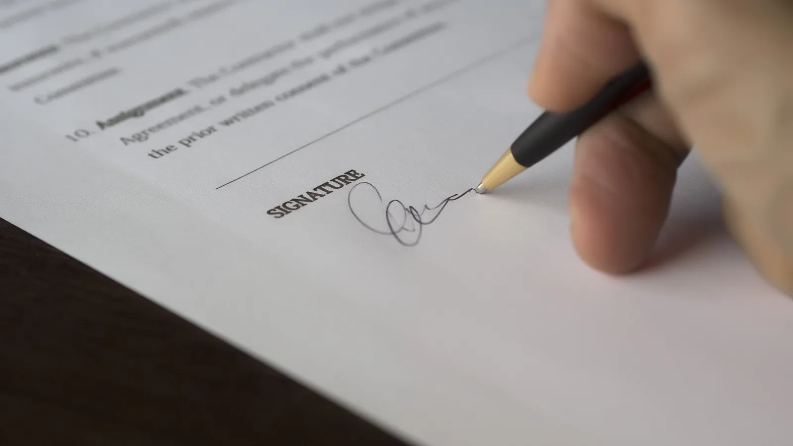 A close-up of a hand signing a paper document with a ballpoint pen