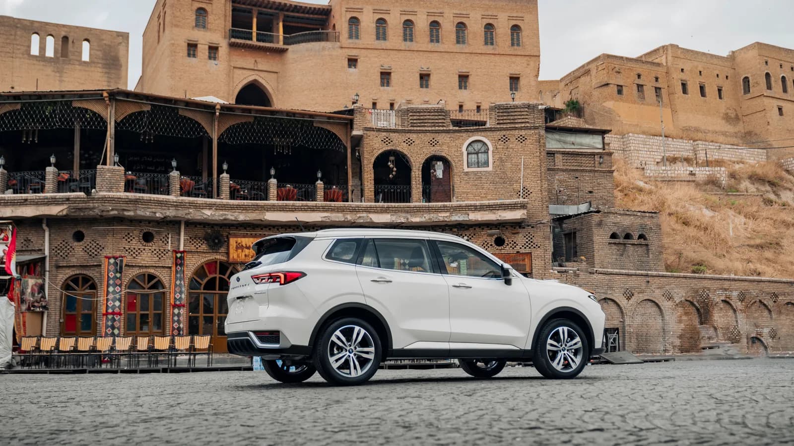 A white small SUV parked in front of old stone buildings, photographed from the side