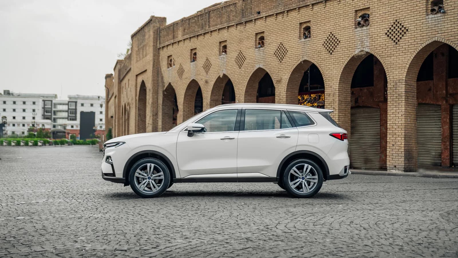 A white small SUV parked in a paved public square, photographed from the side