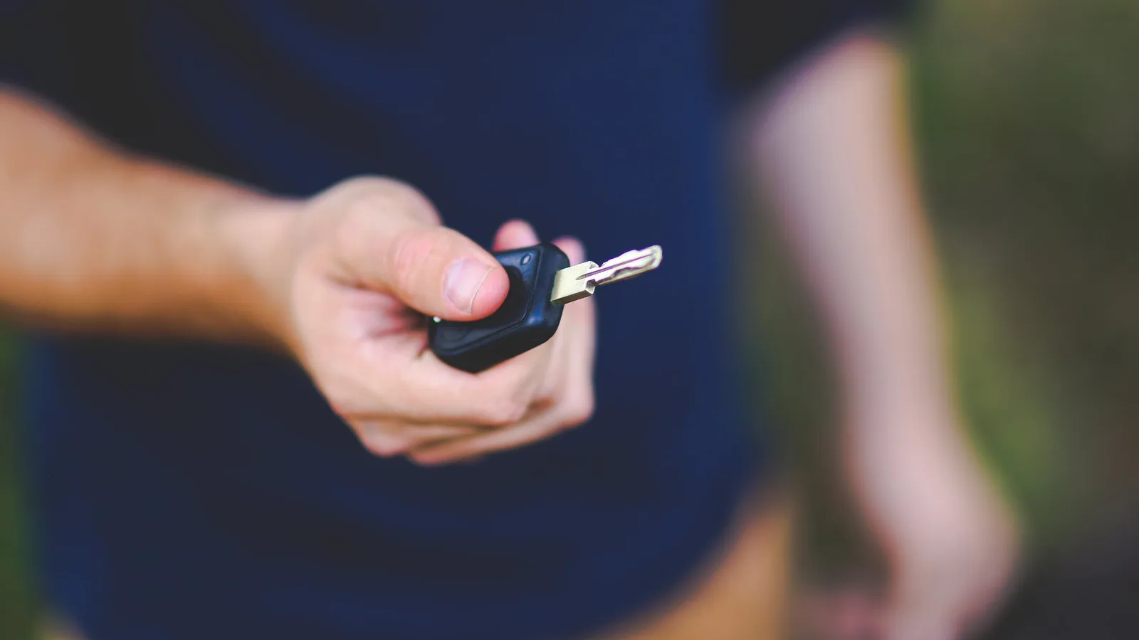 A person in work overalls holding out a car key fob to hand it over