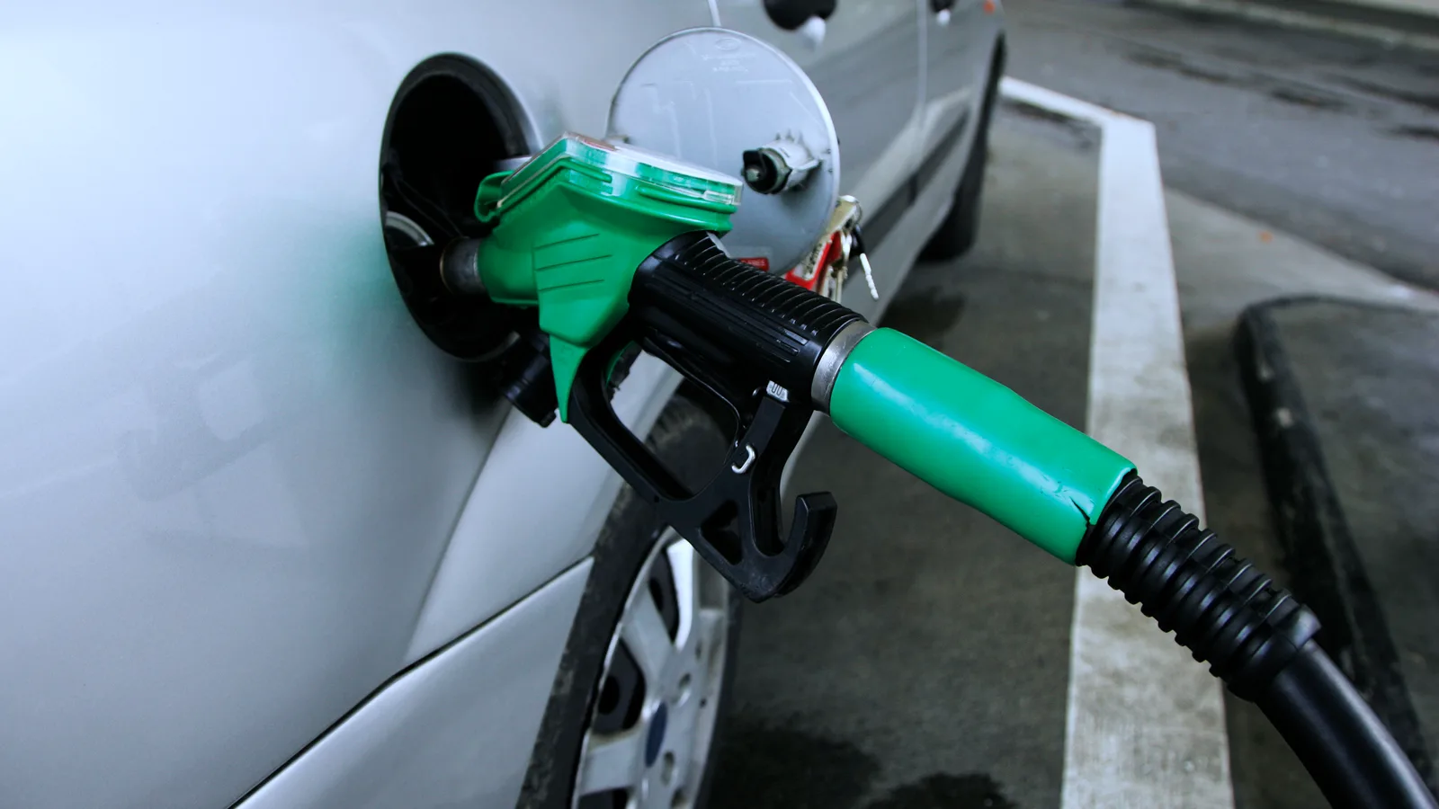 Close view of a green fuel nozzle inserted into the filler neck of a silver car