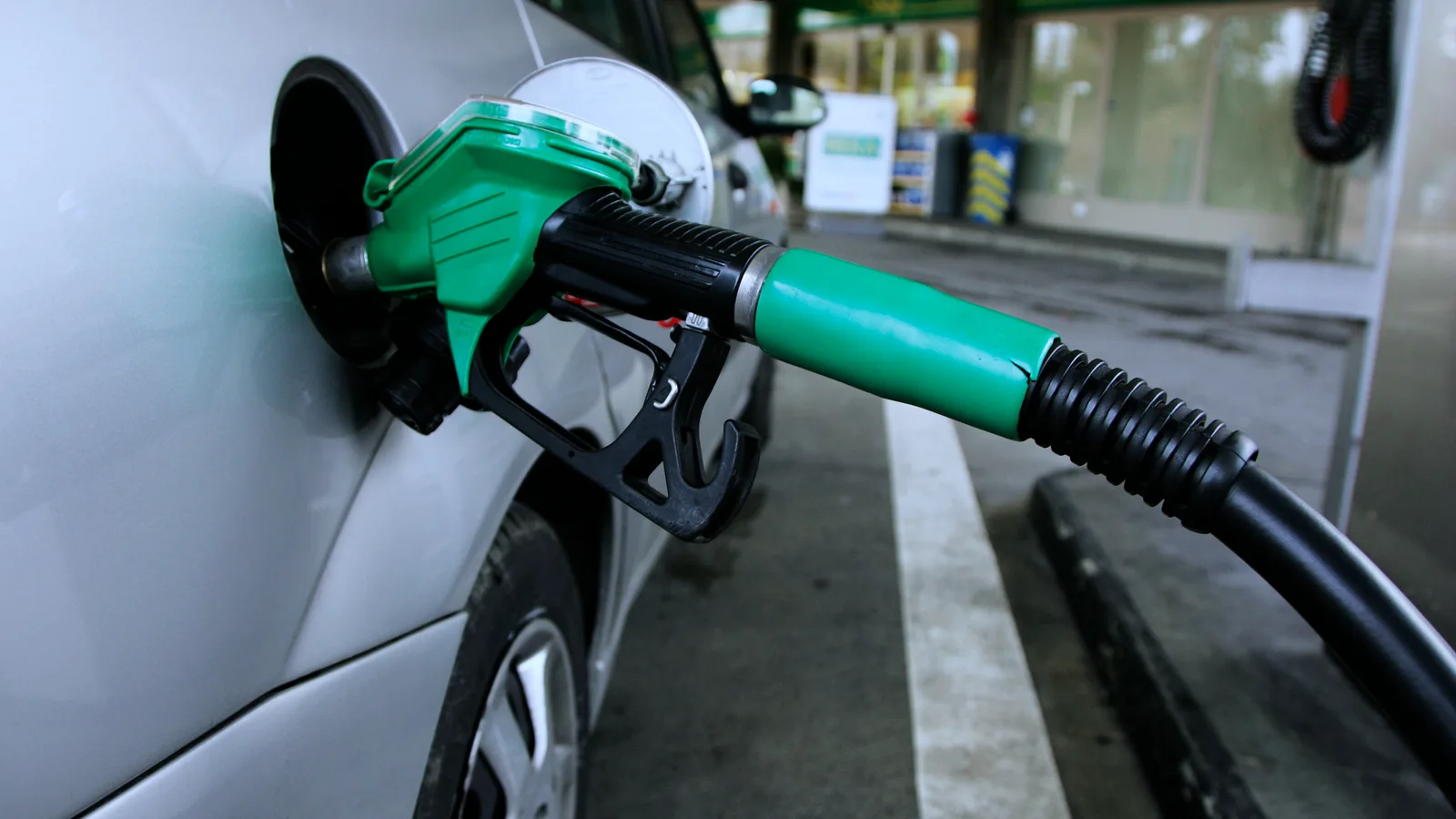 A green fuel nozzle refuelling a silver car on a petrol station forecourt in daylight