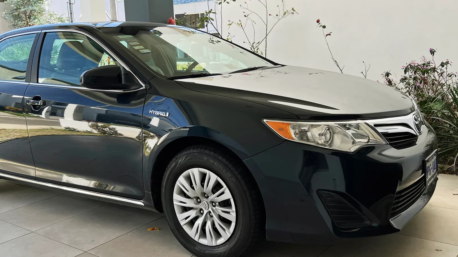 A dark green Toyota Camry Hybrid parked outside a building with its hybrid badge visible