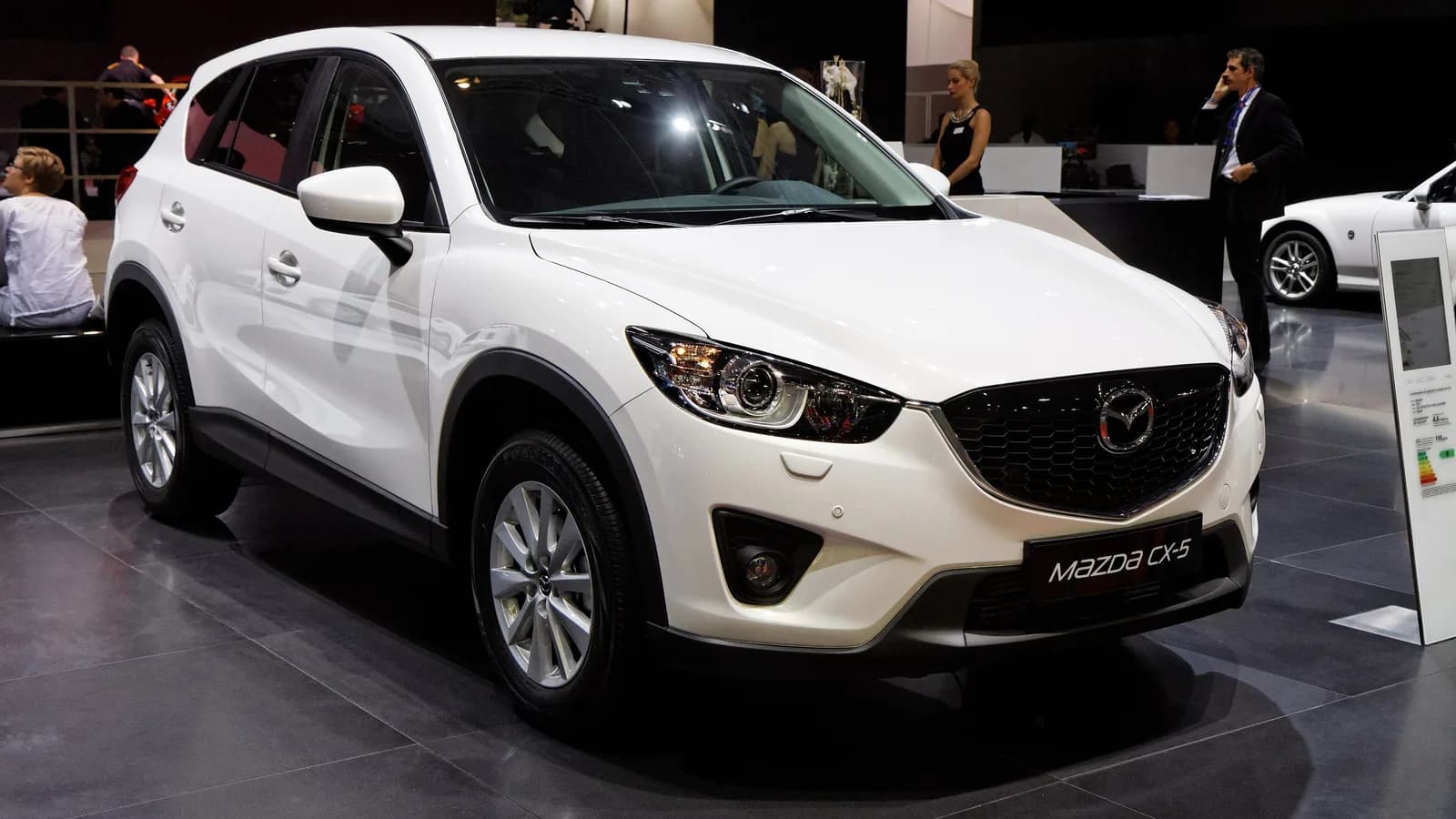 A white Mazda CX-5 petrol SUV on a showroom floor, seen from the front three-quarter angle