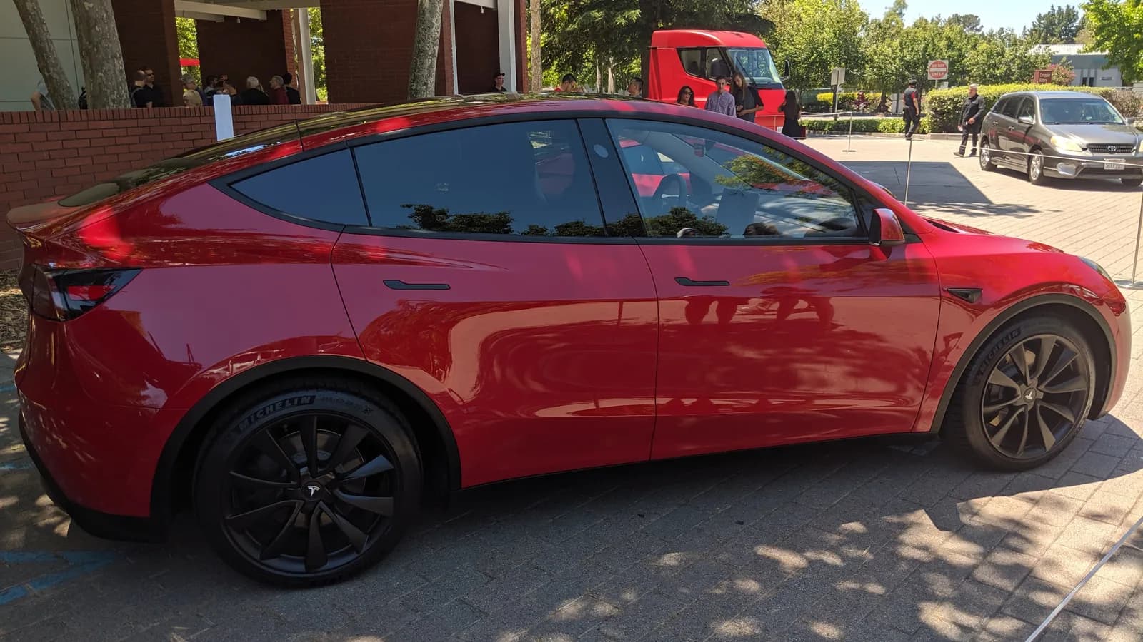 A red Tesla Model Y parked outdoors in bright sunshine, seen from the passenger side