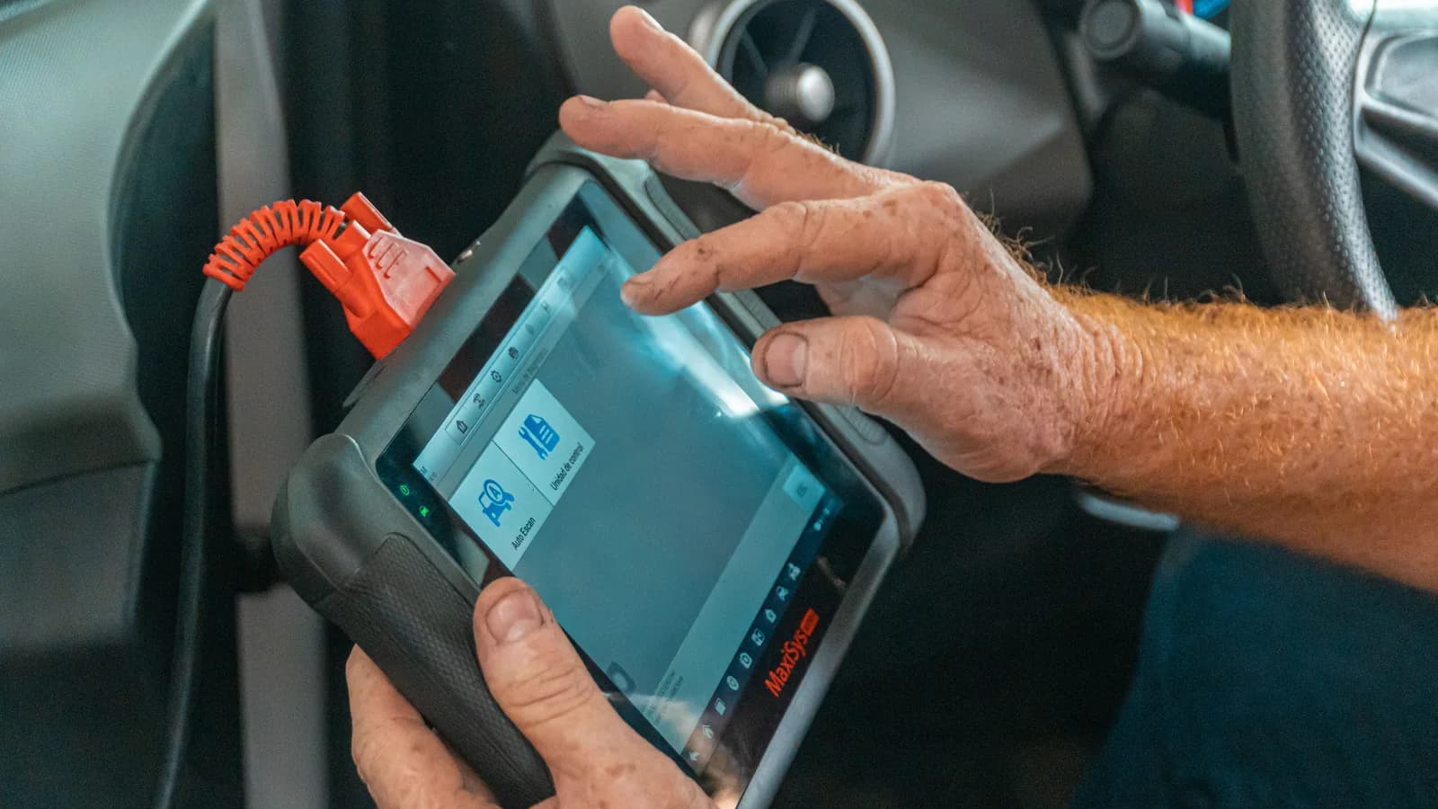 A technician holding a handheld battery diagnostic tester beside a car