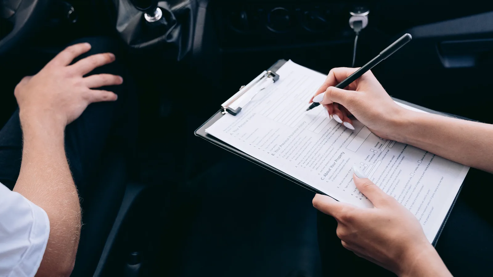 A person sitting in a car filling in a finance form attached to a clipboard