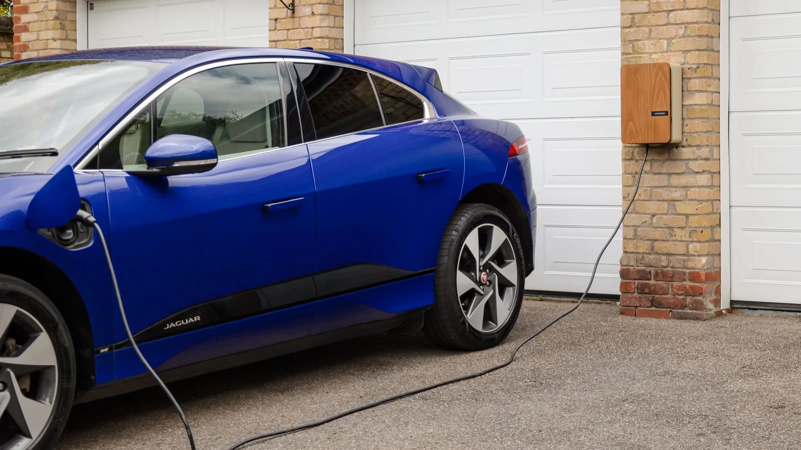 White electric SUV plugged into a charger mounted on a brick house