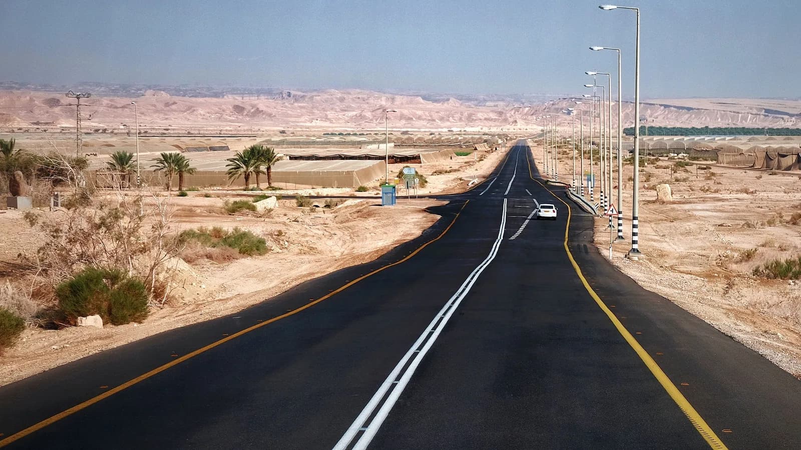 A car on an empty asphalt road running through dry desert scrub under a clear sky