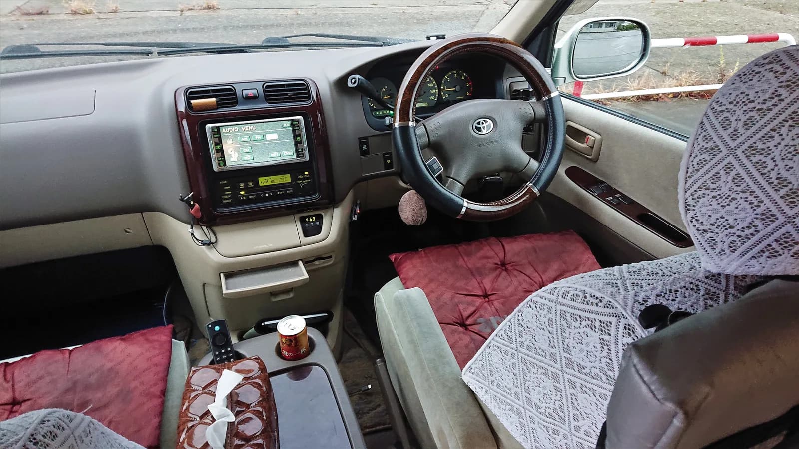 Older Toyota HiAce cabin with a wood-trim steering wheel, aftermarket audio head unit and patterned seat covers