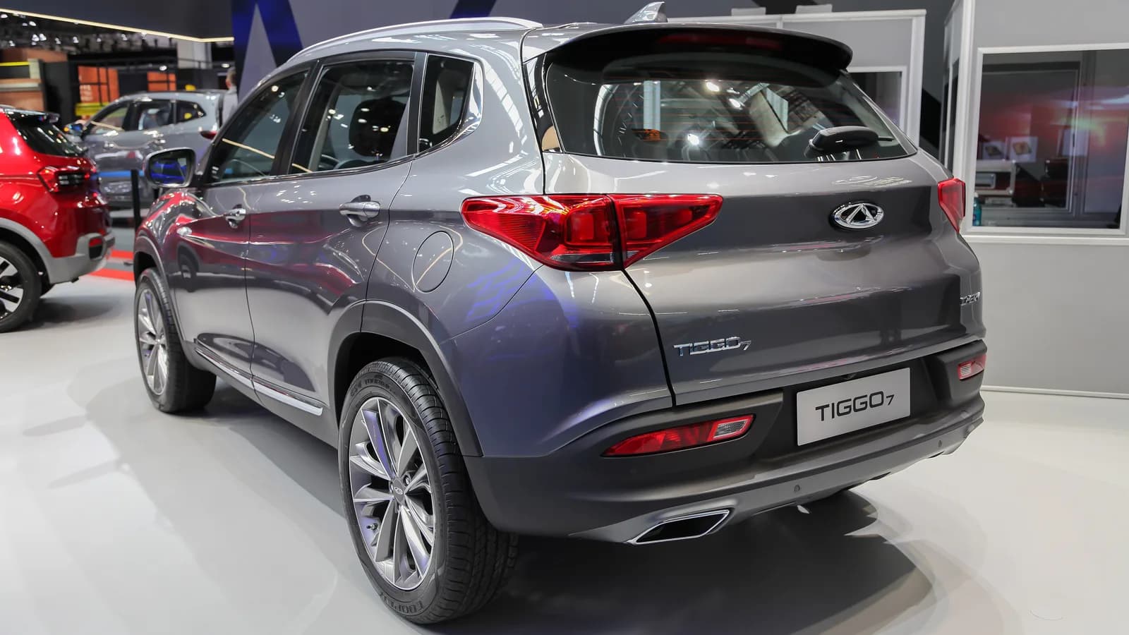 A grey Chery Tiggo SUV seen from the rear three-quarter angle on a motor show floor