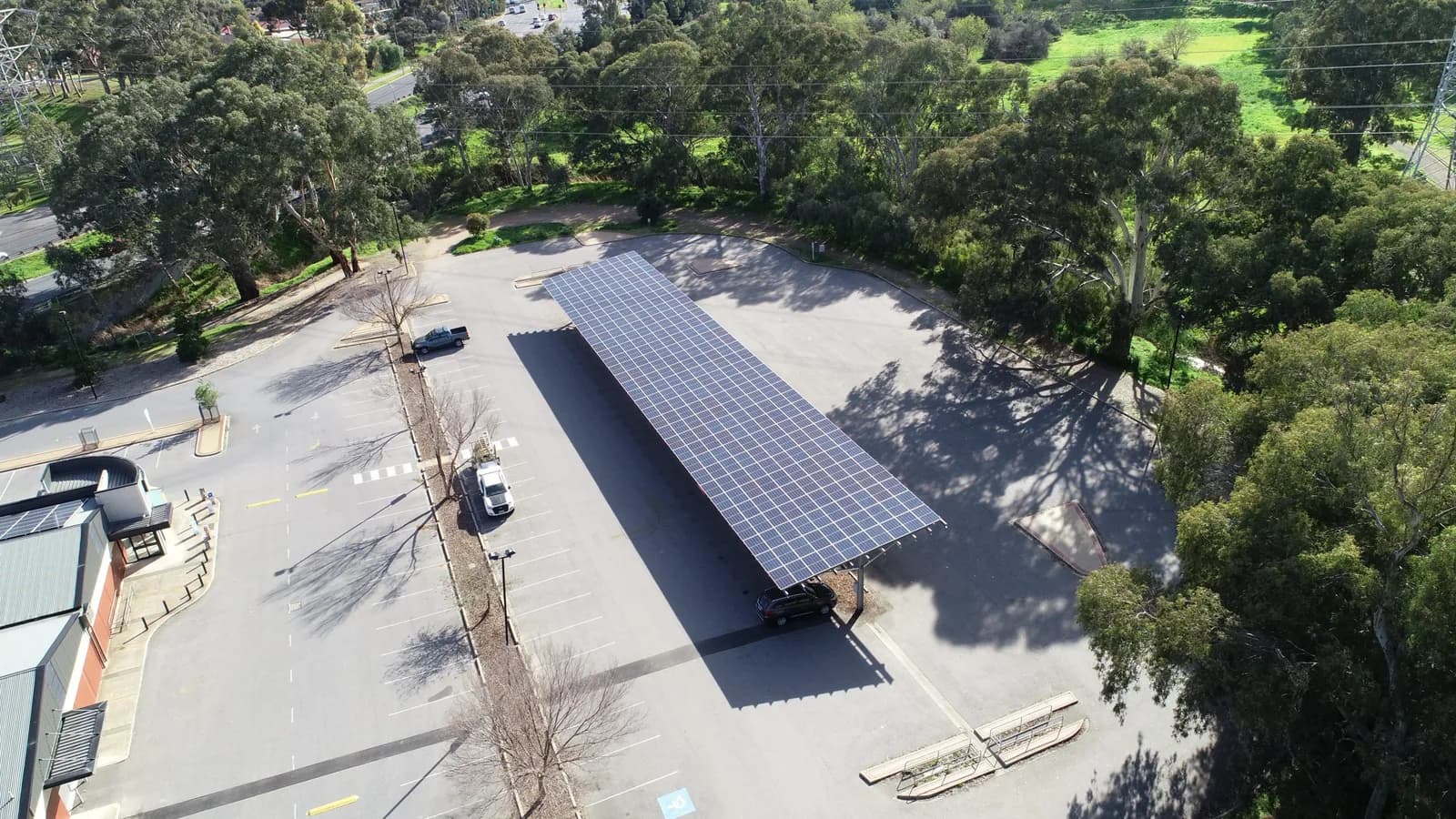 A dark SUV parked underneath a solar panel carport in an open car park, seen from above