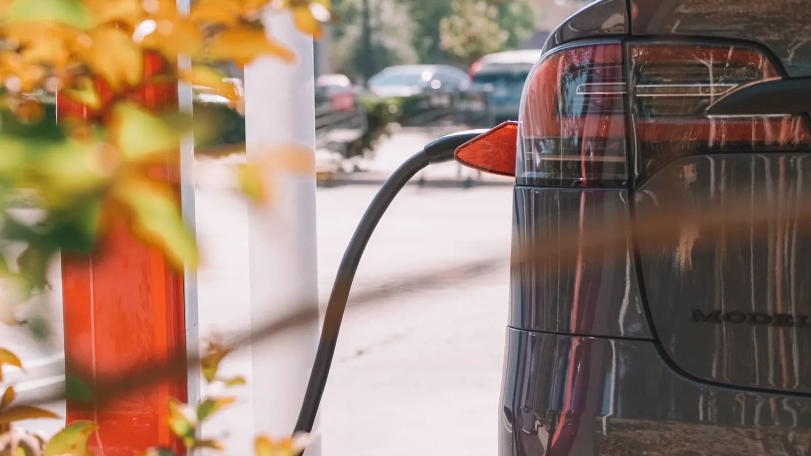 A charging cable plugged into the charge port at the rear of a dark electric car