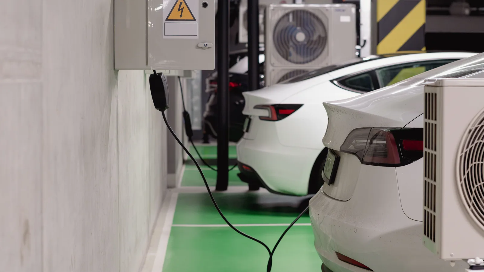Two white electric cars plugged in and charging in a shaded underground car park