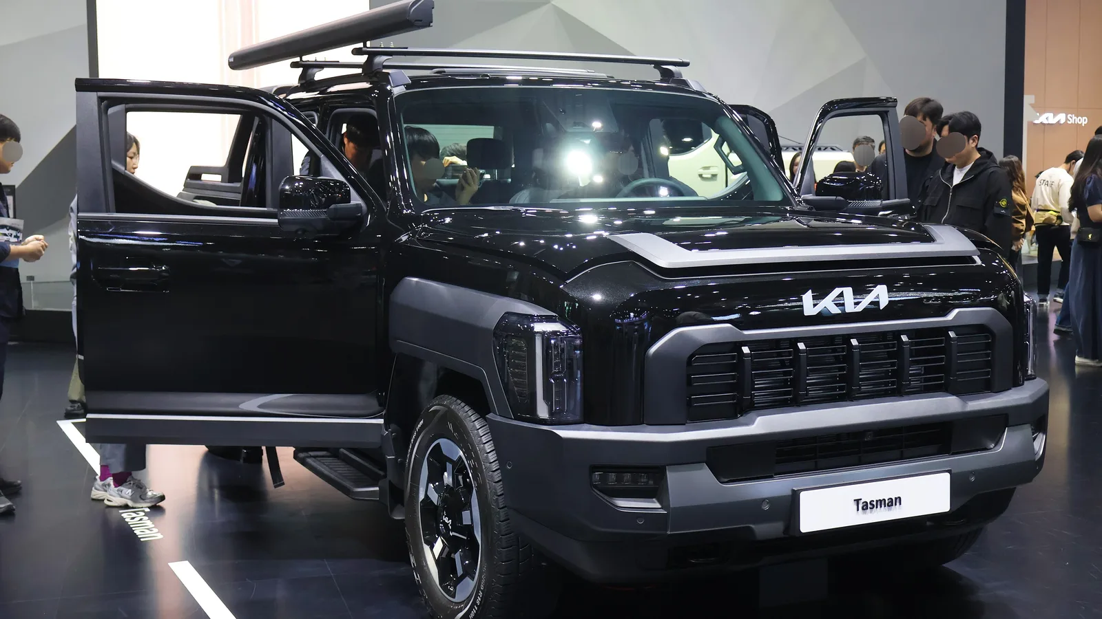 Black Kia Tasman dual-cab ute on a motor show stand with its doors open