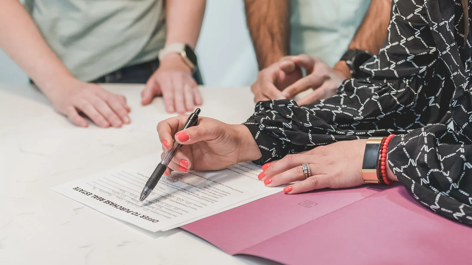 Several people seated around a table while one of them signs a printed agreement