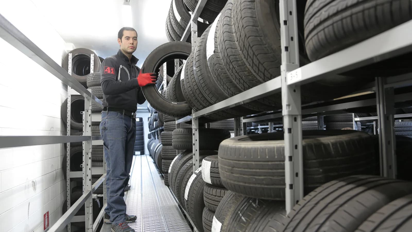 Worker choosing a replacement tyre from racks in a tyre shop