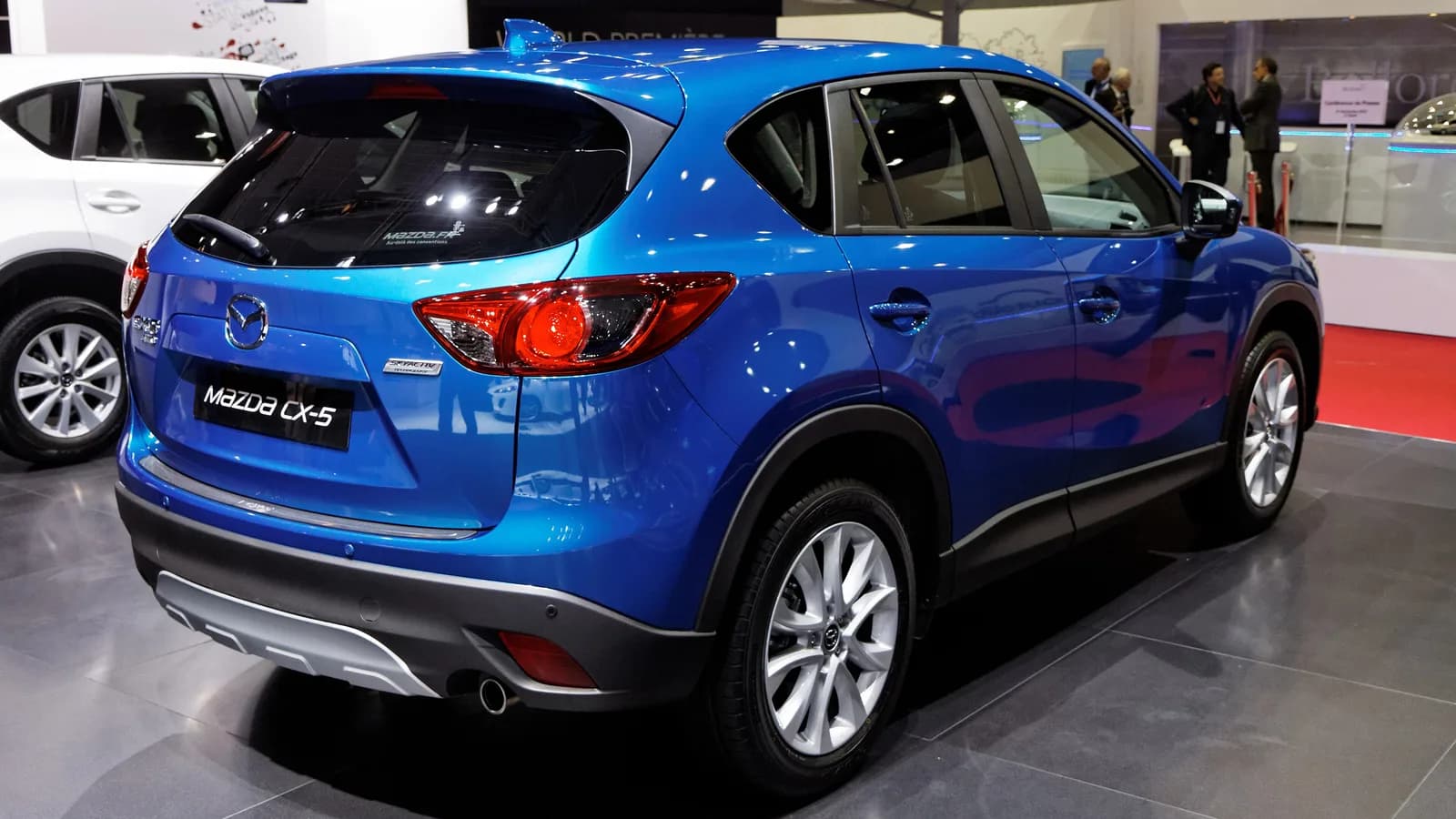 A blue Mazda CX-5 SUV photographed from the rear three-quarter angle on a showroom floor