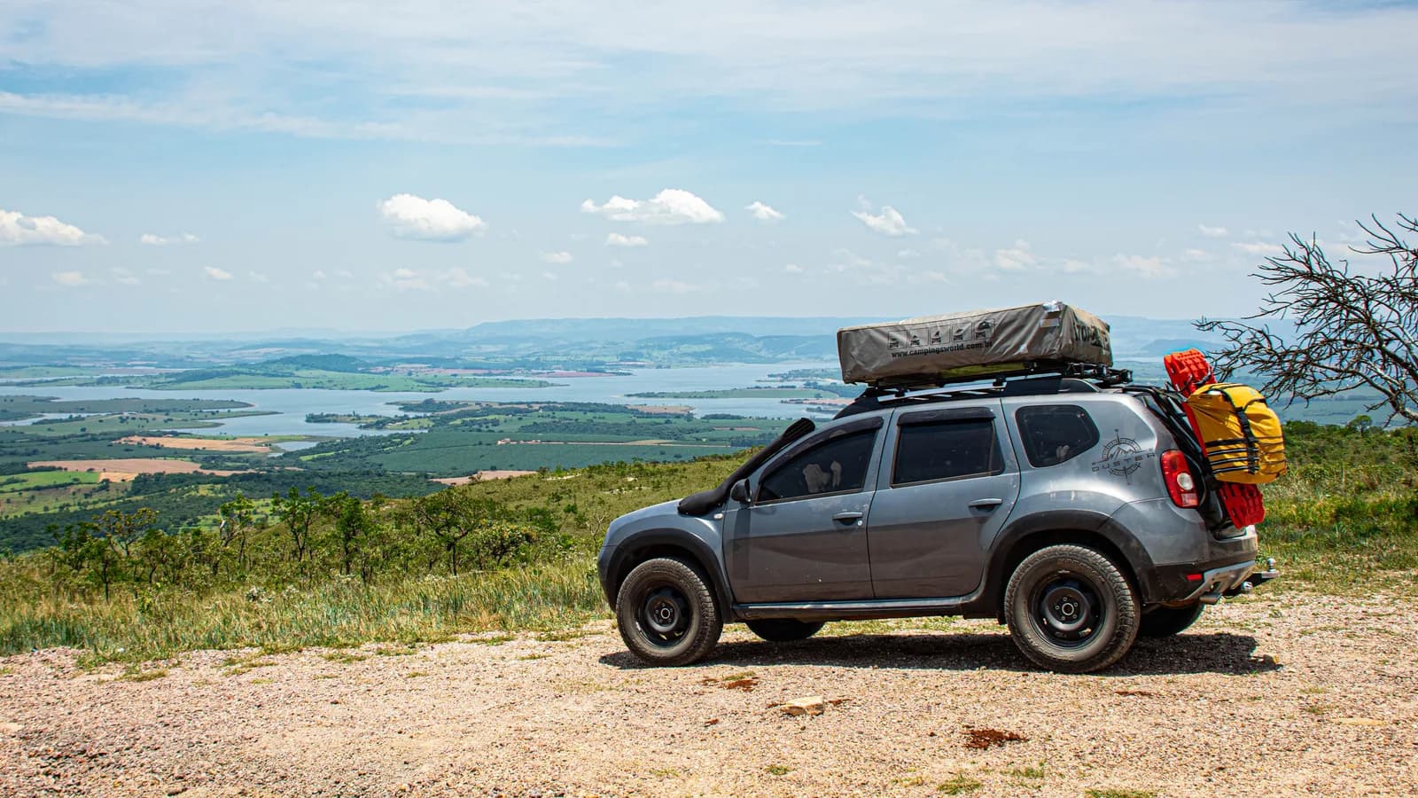 A small SUV carrying a rooftop tent parked on a hilltop overlooking a lake