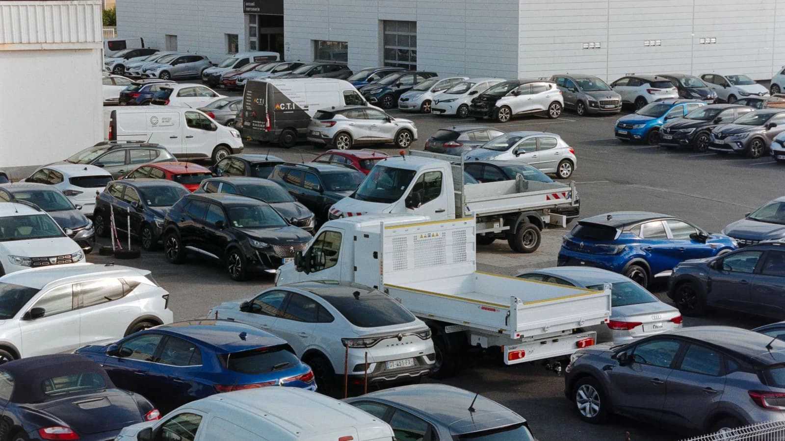An aerial view of a dealership yard filled with parked cars, vans and a small truck