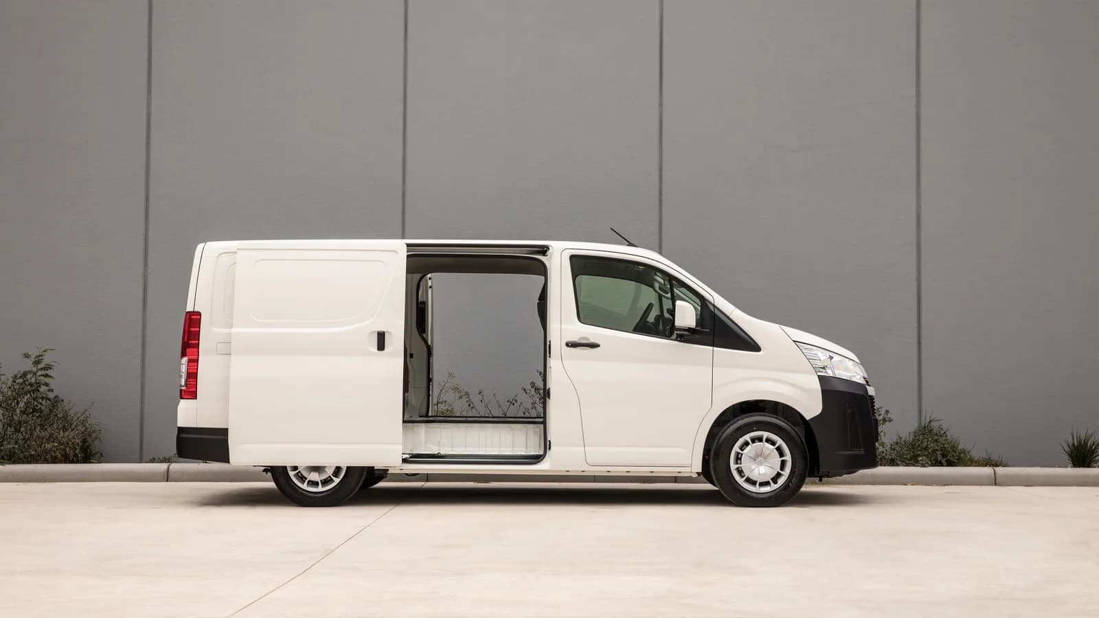 A white HiAce van in side profile with the sliding door open, against a grey wall