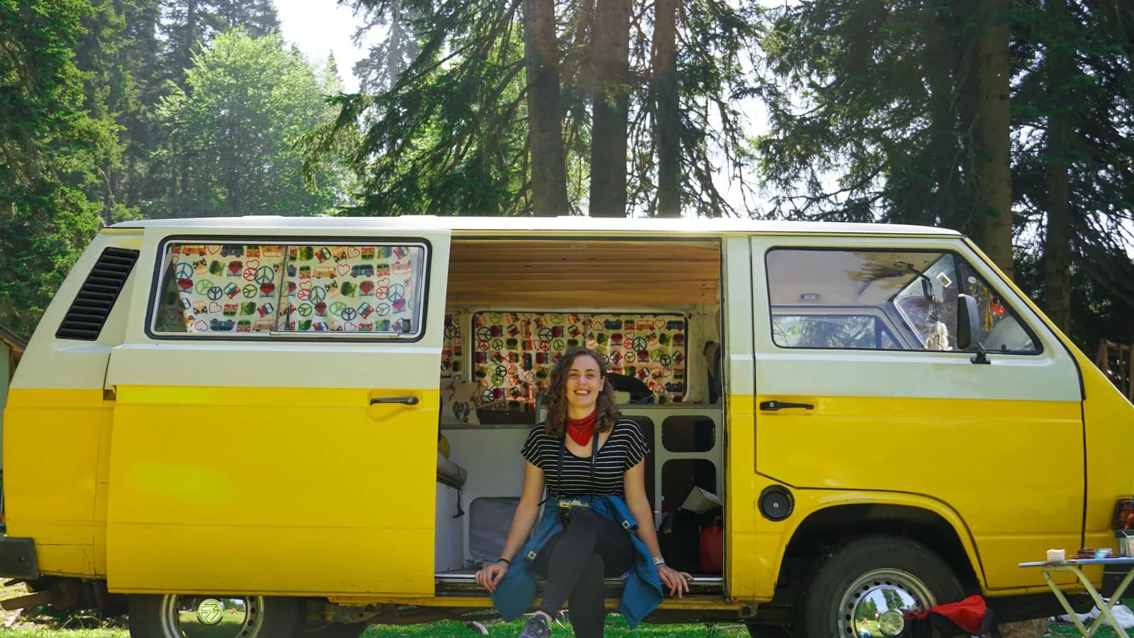 A yellow campervan parked among trees at a bush campsite with its sliding door open