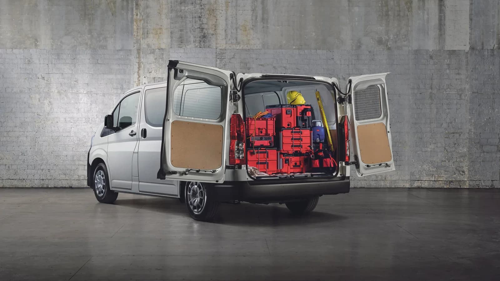 A white Toyota HiAce with its rear doors open, the cargo bay loaded with red tool cases and a hard hat
