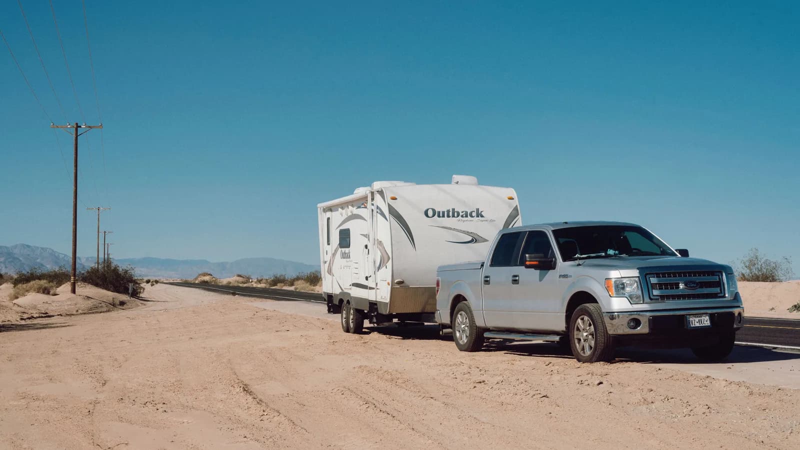 A silver ute towing a caravan along a straight, dry outback road