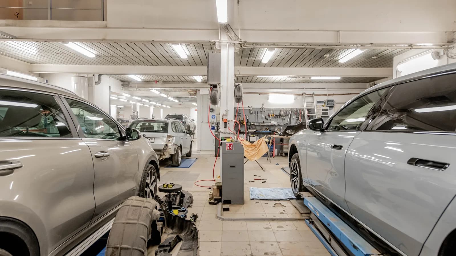 Several cars raised on hoists and parked on the floor of a busy vehicle service centre