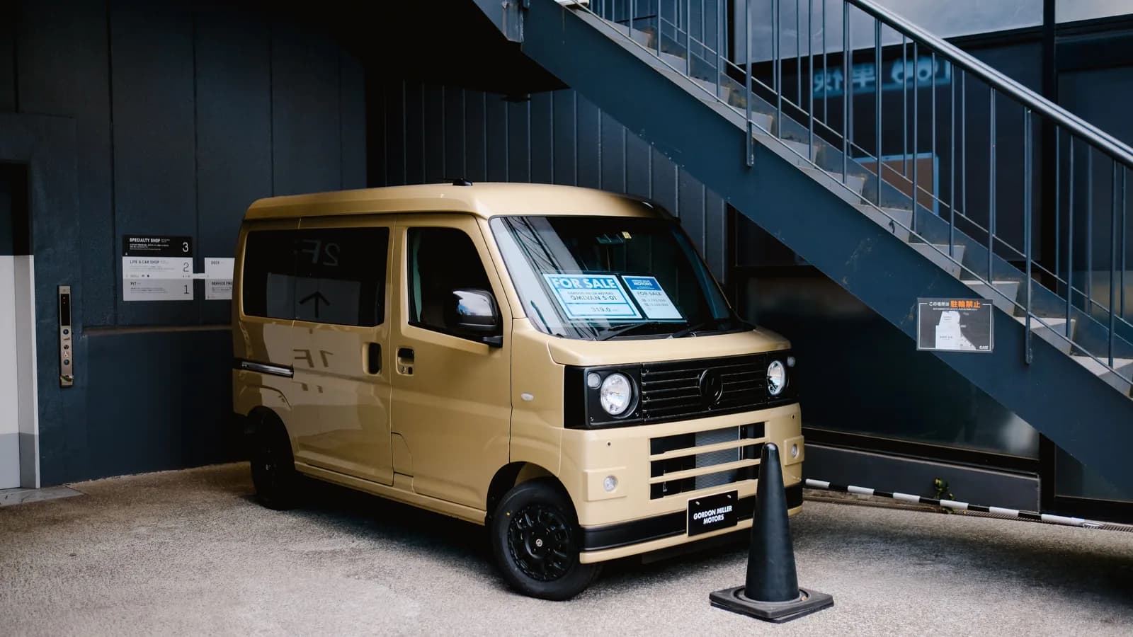 A small gold van with for sale signs in the windscreen parked outside a building