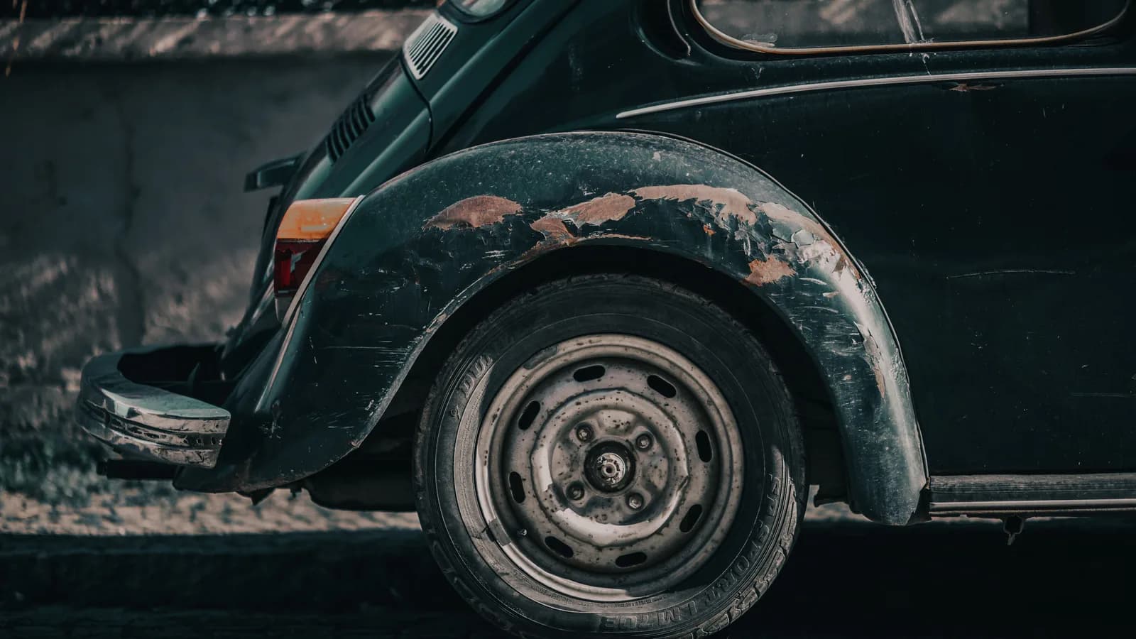 Rust and peeling paint around the rear wheel arch of an older green car