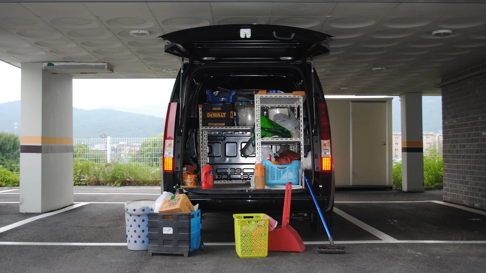 The open rear doors of a van showing shelving, tools and camping gear stacked inside