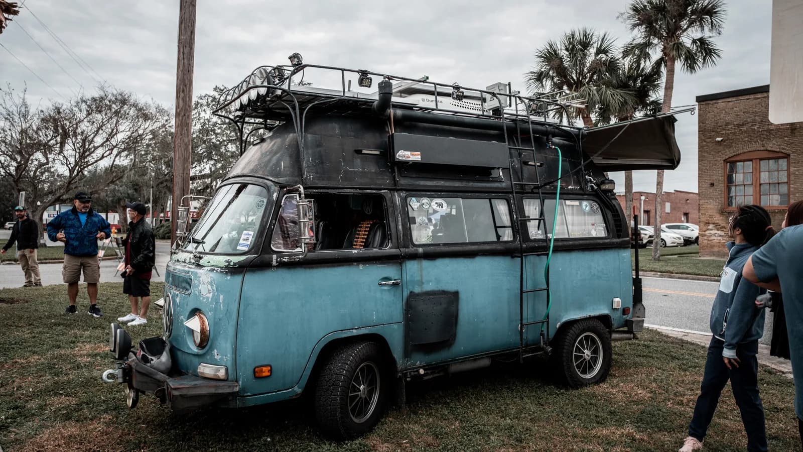 A converted camper van on grass with a roof rack, ladder and awning extended