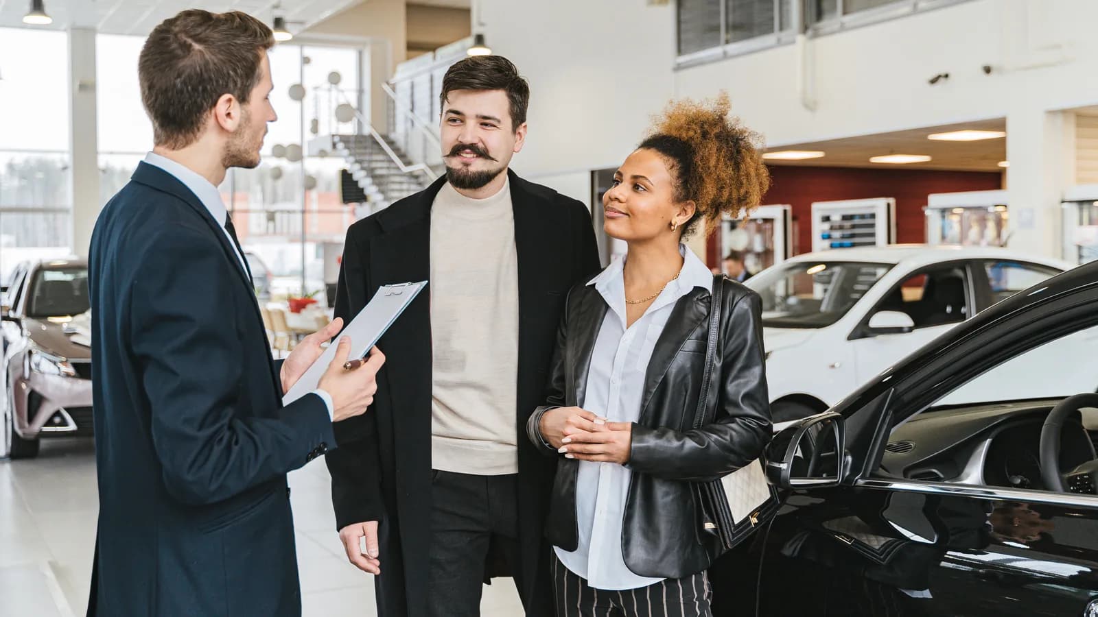 A salesperson talking with a couple beside a black car in a dealership showroom