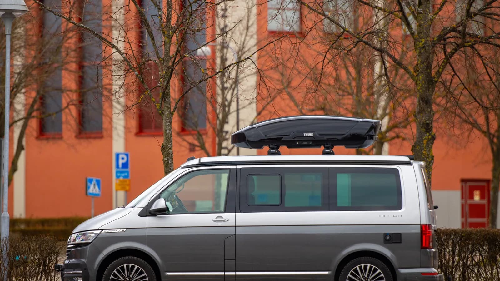 A silver van fitted with a roof cargo box parked against the kerb