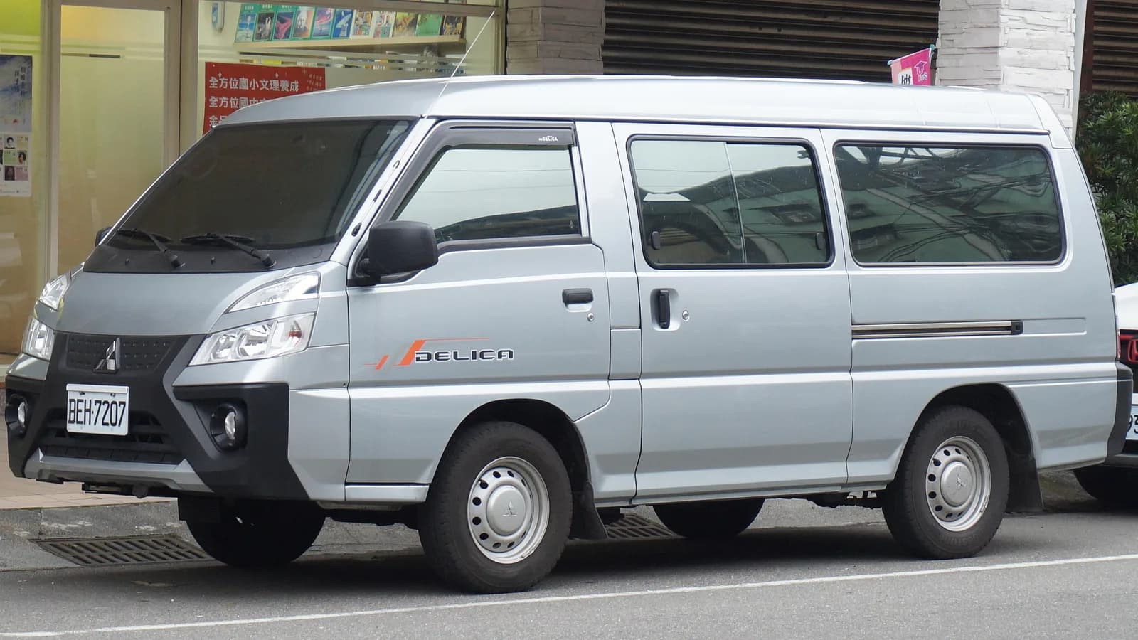 A silver Mitsubishi Delica van parked on a street, seen from the front three-quarter angle