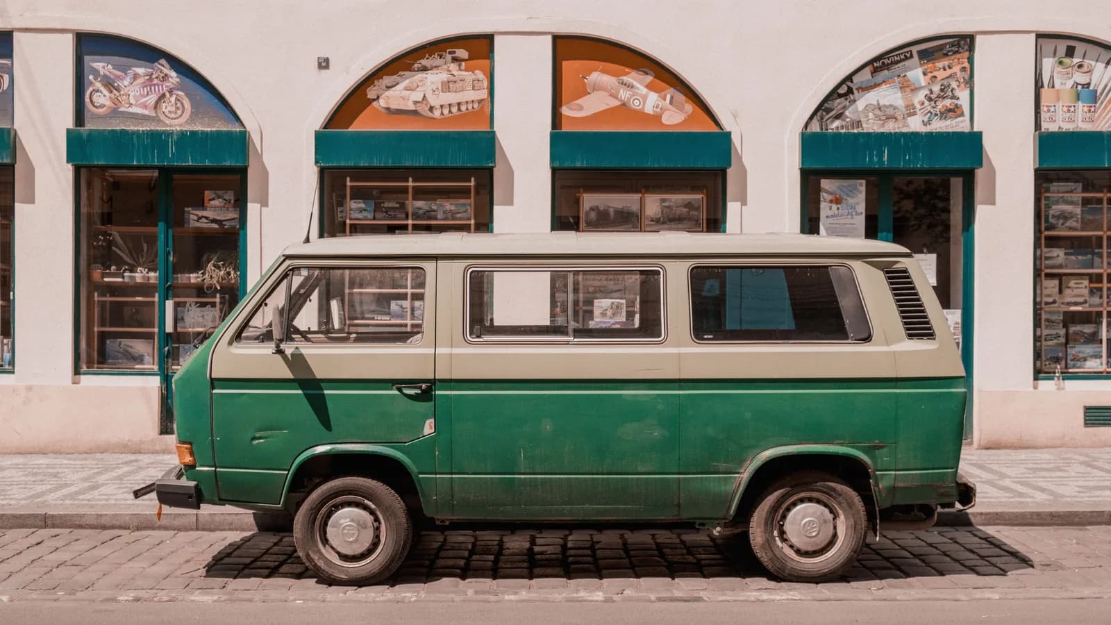 An older two-tone campervan parked on a cobblestone street outside a row of shopfronts