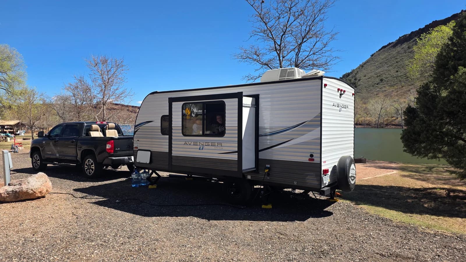 A dark ute towing a caravan at a lakeside campsite