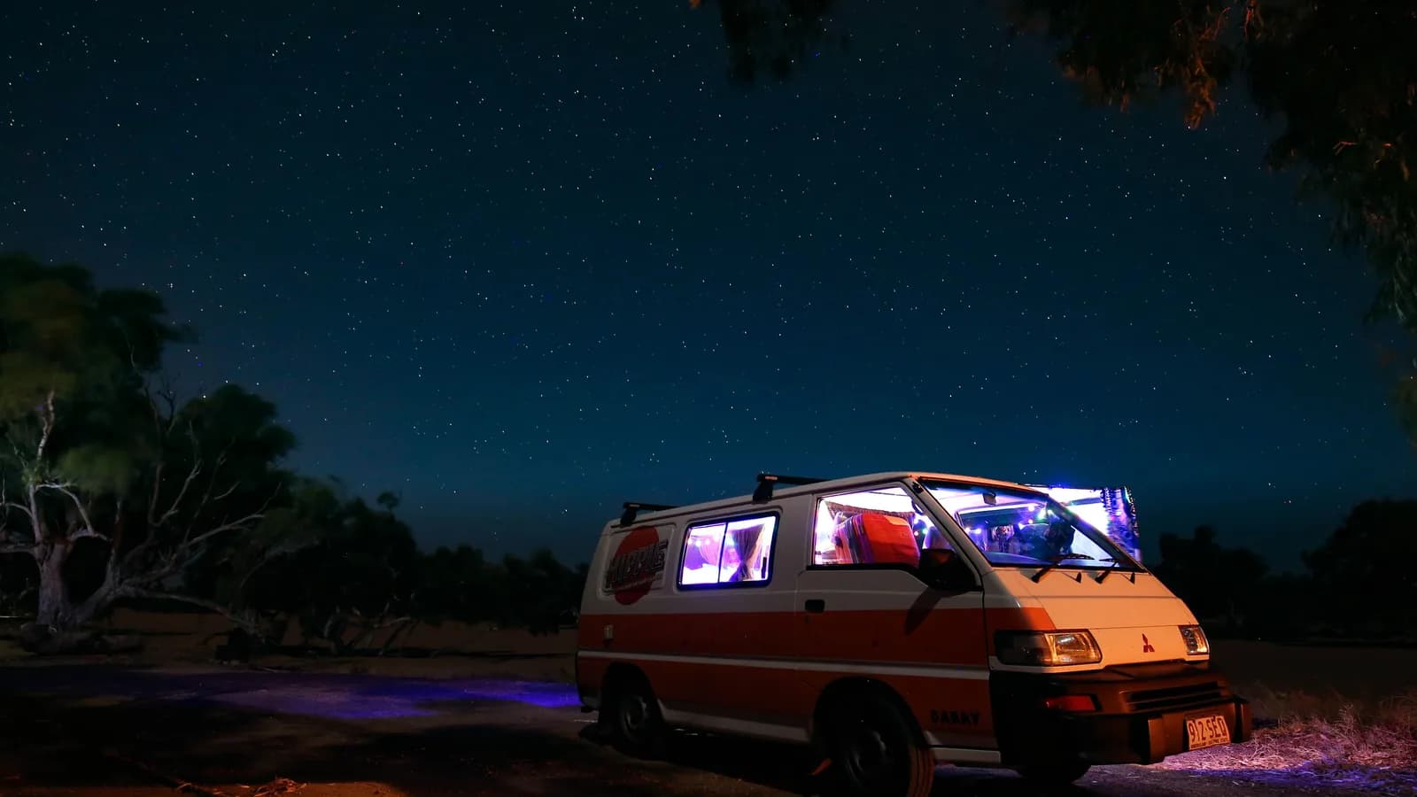 A camper van with its interior lights on, parked in open country under a starry night sky