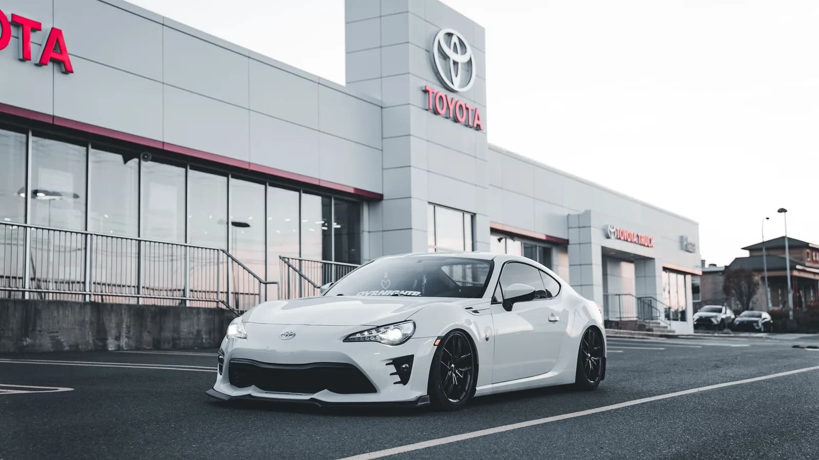 A white sports car parked on a dealership forecourt in front of the showroom windows