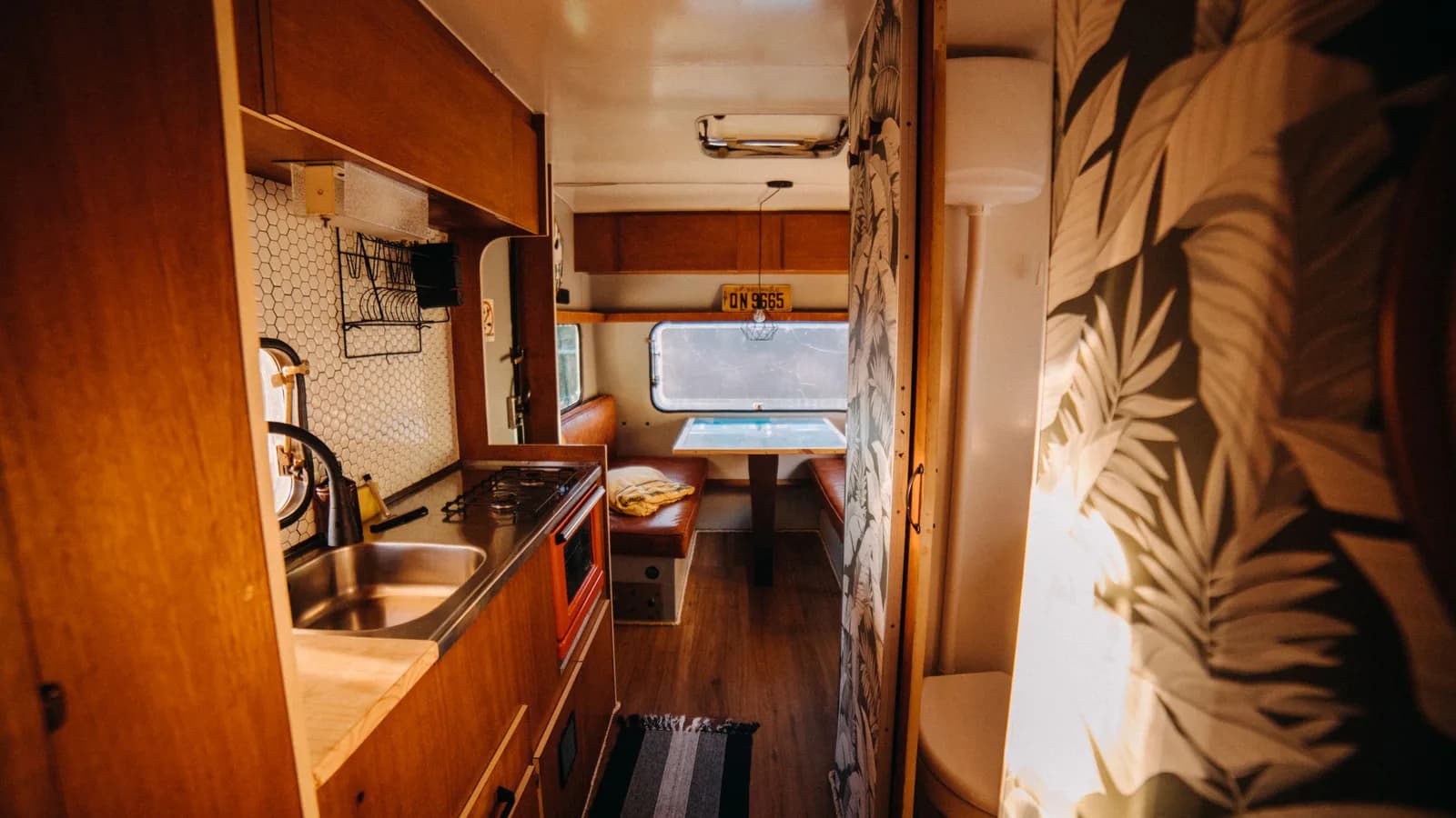 A van kitchen with timber cabinets, a sink, a stovetop and a small dining table