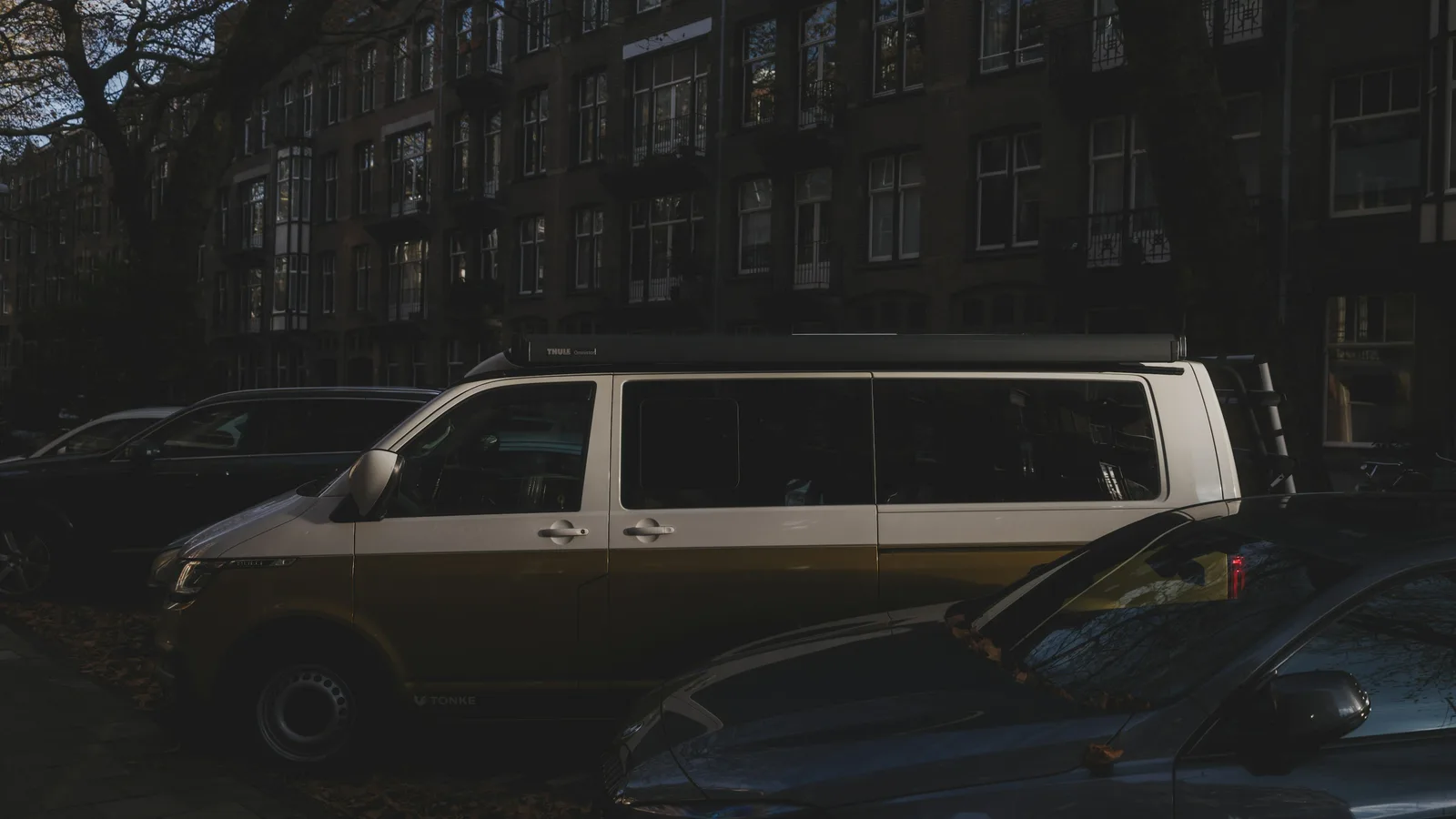 A converted camper van with a rooftop tent parked among cars on a suburban street at dusk