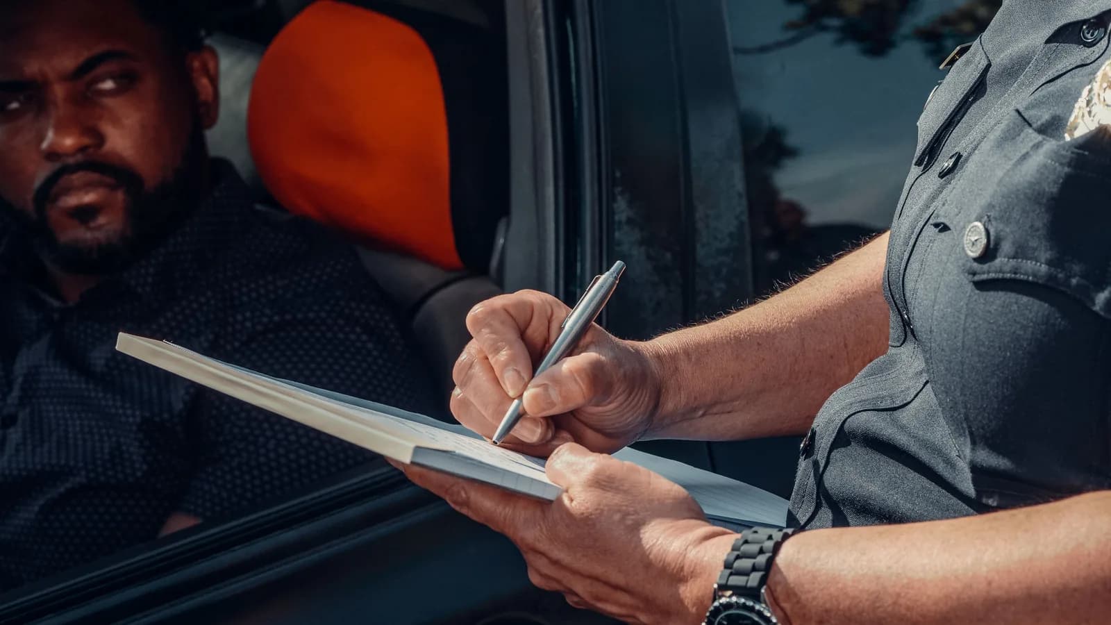 A police officer writing on a clipboard at a driver's window during a roadside stop