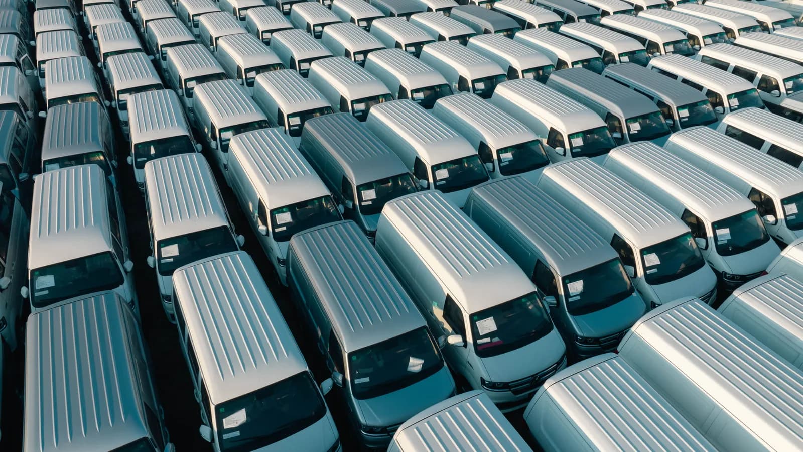 Rows of white cargo vans parked in a storage lot seen from above