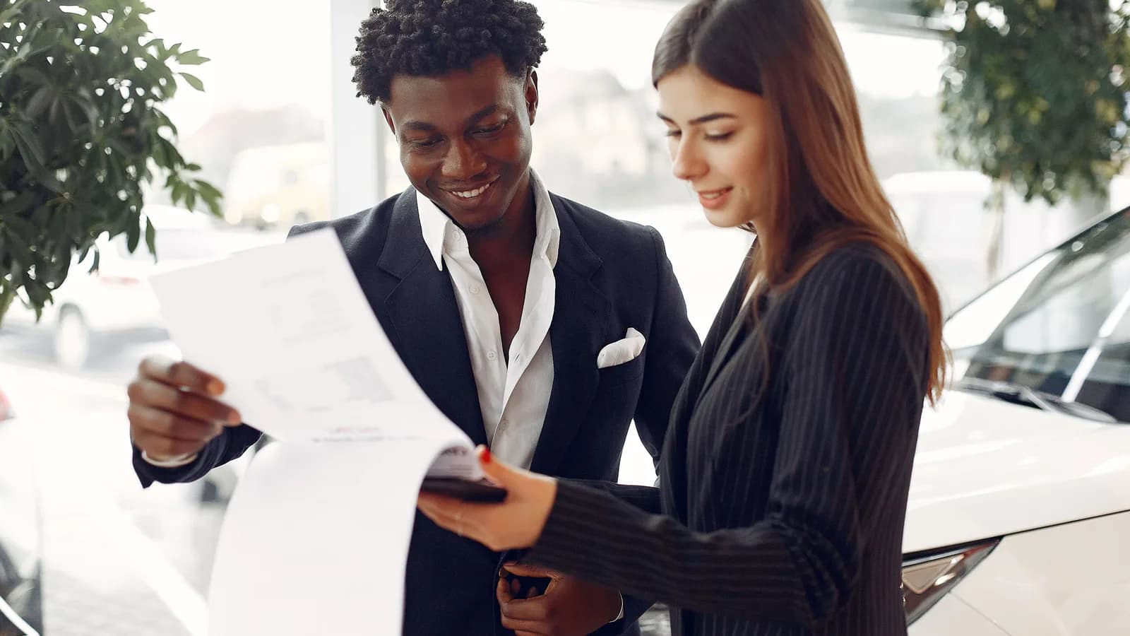 Two people checking a written sales agreement beside a white car