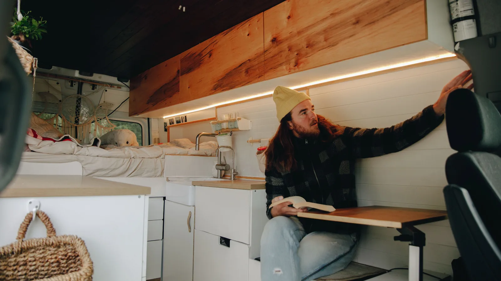A man standing in the kitchen area of a fitted-out campervan with timber cabinetry and a sink