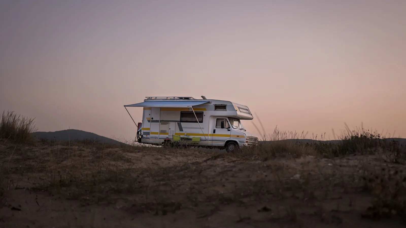 A campervan with its awning out, parked on sand at dusk