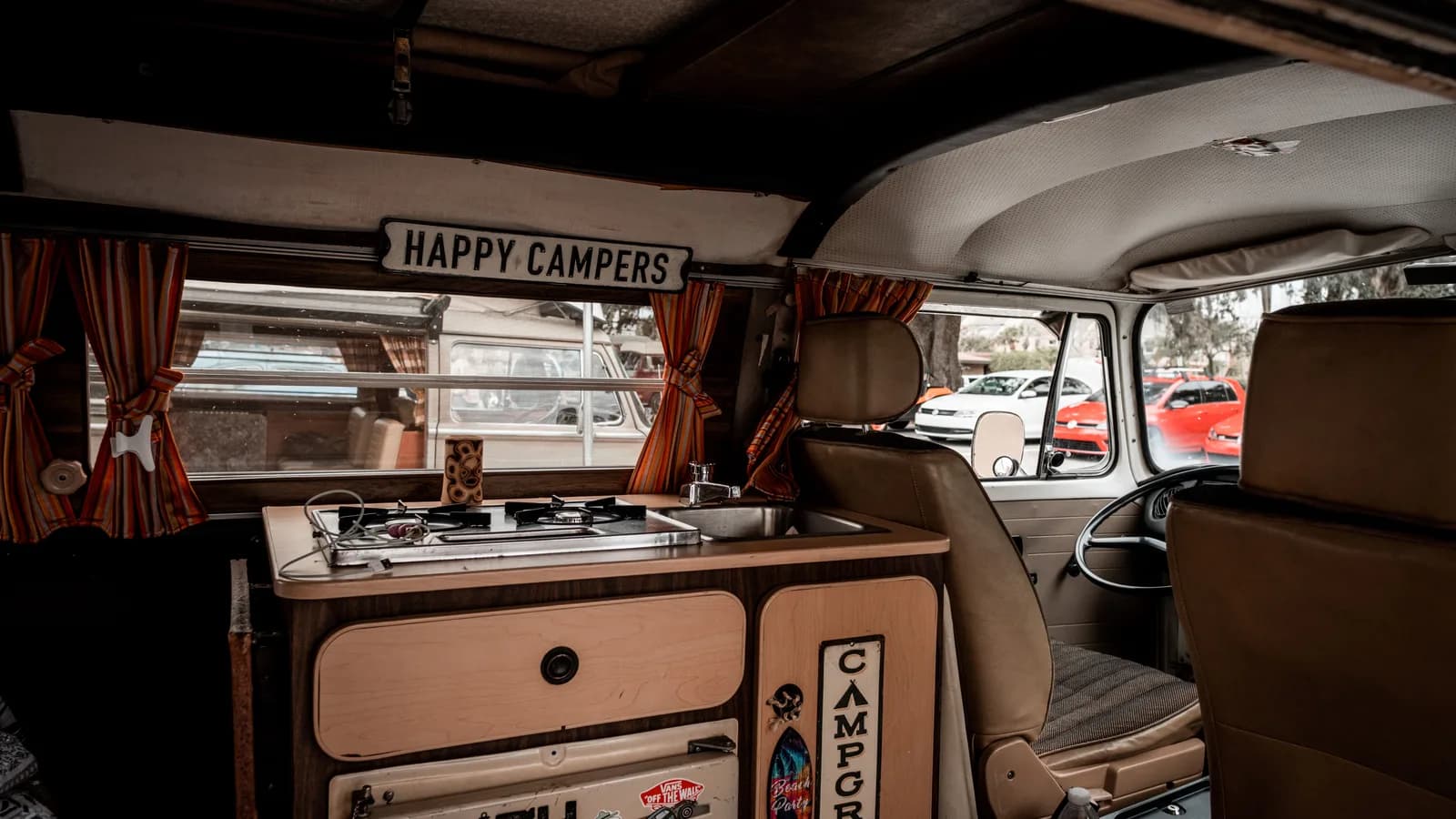 A compact camper kitchen unit with a two-burner gas hob and a small sink inside a vintage van