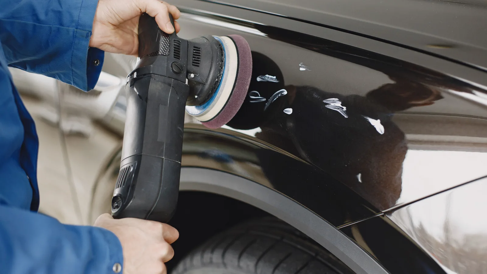 A technician polishing scratches from the rear panel of a black car